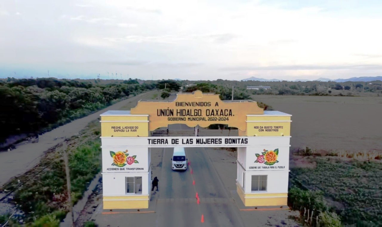 Entrada al municipio de Unión Hidalgo, Oaxaca, con un arco amarillo que da la bienvenida a los visitantes, rodeado de paisajes naturales y aerogeneradores en el fondo.